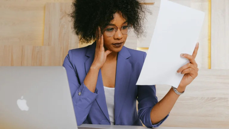woman in blazer with laptop and paper in hand