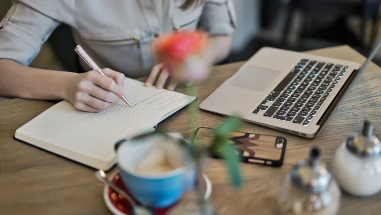 woman writing with laptop and coffee cup