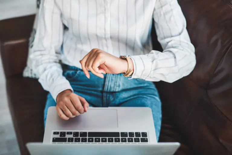 Cropped shot of a woman using a laptop on the sofa and checking the time while working from home