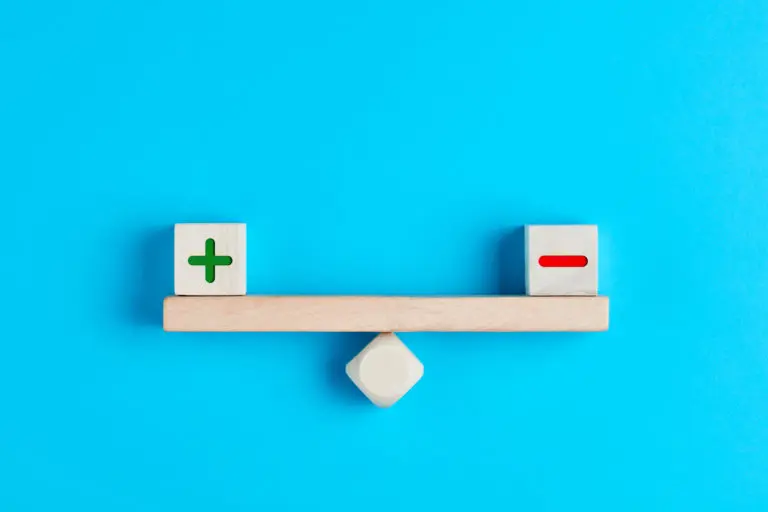 Plus and minus or positive and negative symbols on wooden blocks are in balance on a wooden seesaw. Blue background, flat lay view. Pros and cons equilibrium in decision making under uncertainity.