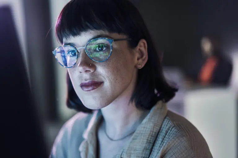 woman with glasses looks at computer screen