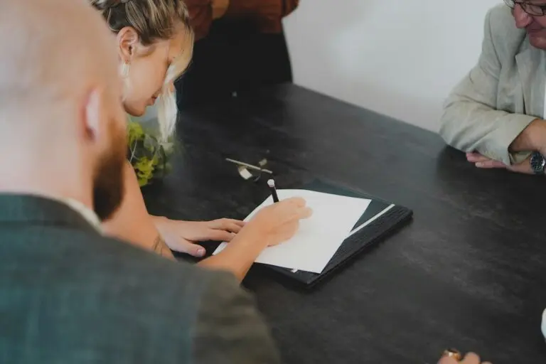 woman signs legal document with male partner sitting beside her